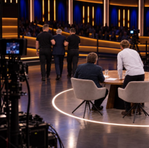 Televisiestudio waar twee medewerkers een deelnemer van het podium begeleiden